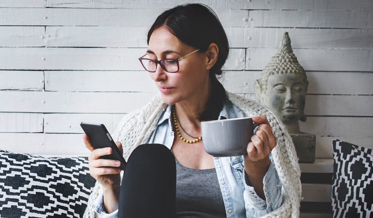 Woman using phone while relaxing and sipping coffee