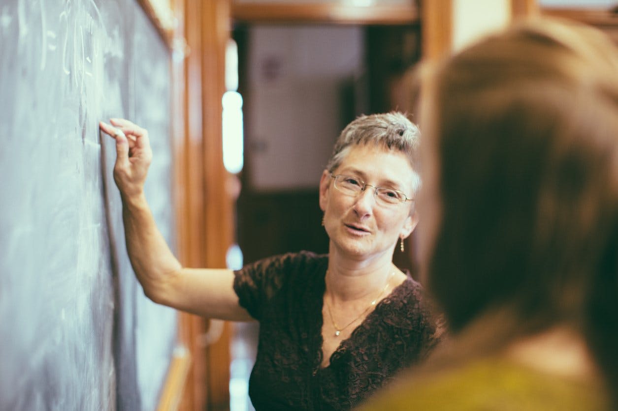 A teacher writing on a chalkboard while talking to a student