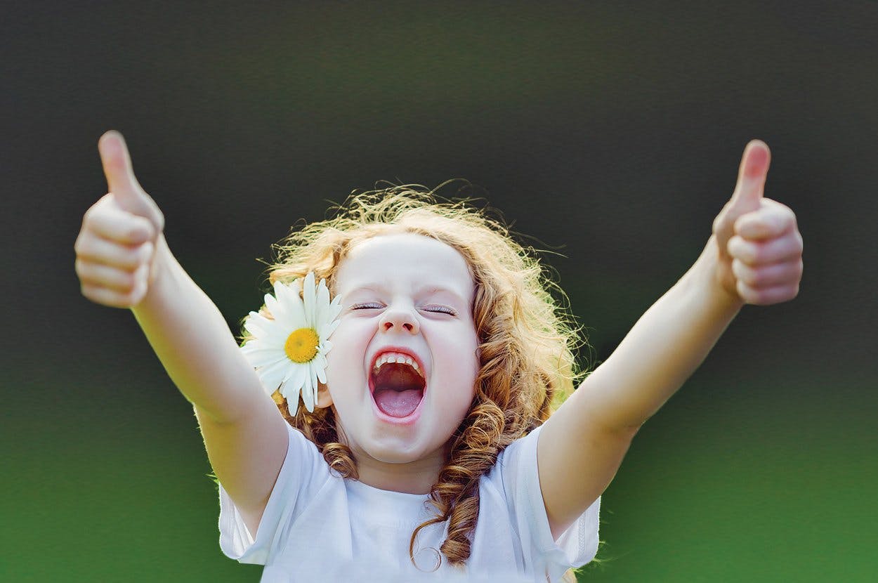 niña feliz con flor en el cabello muestra sus pulgares hacia arriba